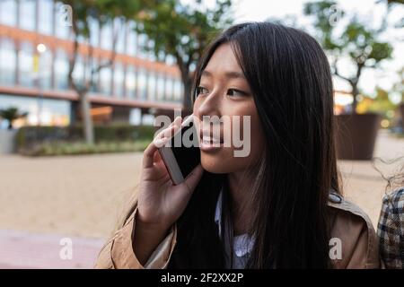 Asiatische Frau in stilvollem Outfit stehen auf der Straße und sprechen Telefon Stockfoto