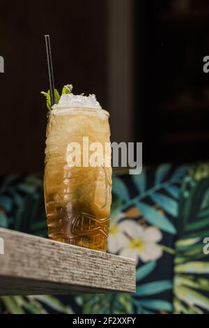 Tiki Tasse mit kaltem Alkoholgetränk mit Stroh serviert mit Eis und dekoriert mit frischem Kraut auf verschwommenem Hintergrund platziert Stockfoto