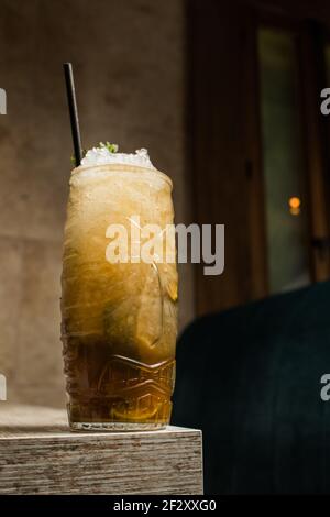 Tiki Tasse mit kaltem Alkoholgetränk mit Stroh serviert mit Eis und dekoriert mit frischem Kraut auf verschwommenem Hintergrund platziert Stockfoto