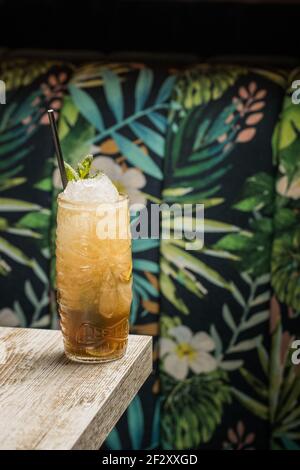 Tiki Tasse mit kaltem Alkoholgetränk mit Stroh serviert mit Eis und dekoriert mit frischem Kraut auf verschwommenem Hintergrund platziert Stockfoto