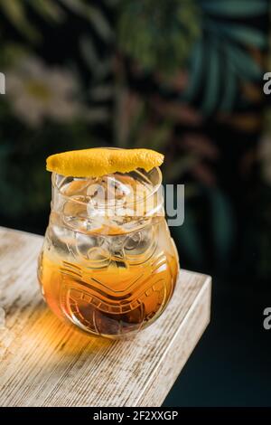 Von oben Tiki Glas Tasse mit Alkohol auf gelegt Rand von Holztisch im Zimmer mit bunten Vorhang auf Unscharfer Hintergrund Stockfoto
