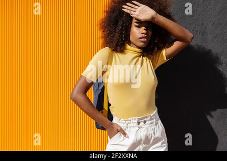Junge ethnische Weibchen mit Afro-Frisur auf gelb und stehen Schwarze Wand und Blick auf die Kamera Stockfoto