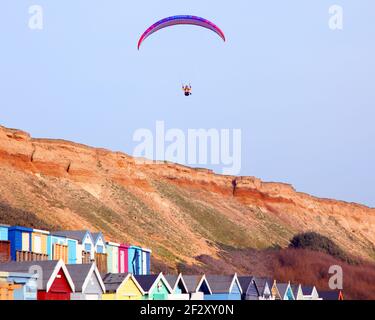 Gleitschirmfliegen im blauen Himmel über Klippen und bunten Strandhütten von Barton on on Sea, Hampshire Stockfoto