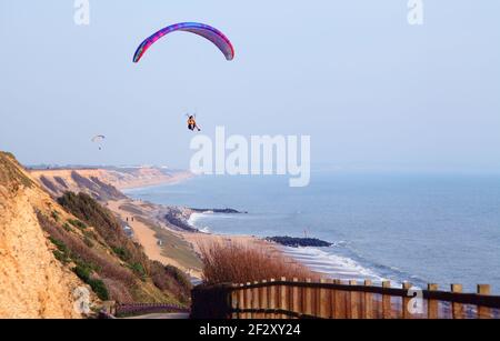 Gleitschirmflieger Paragliding in einem blauen Himmel über Clifftop und Strand in Barton on Sea, Hampshire Stockfoto