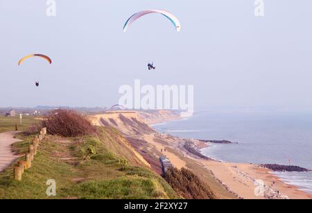 Gleitschirmflieger Paragliding in einem blauen Himmel über Clifftop und Strand in Barton on Sea, Hampshire Stockfoto