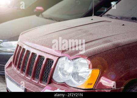 Motorhaube mit Kühlergrill und Scheinwerfer eines roten schmutzigen Autos Blick auf Teile des Autos in einer Schicht von trockenem Staub Nahaufnahme, niemand. Stockfoto