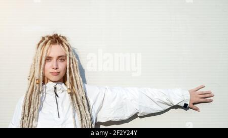 Junge moderne modische Frau mit blonden Dreadlocks Haar zeigt mit Ihre Hand an der Wand Stockfoto