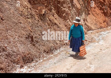 Indigene ältere peruanische Quechua Frau mit traditionellem Hut von Maras auf einem Feldweg in den Anden, Provinz Cusco. Stockfoto