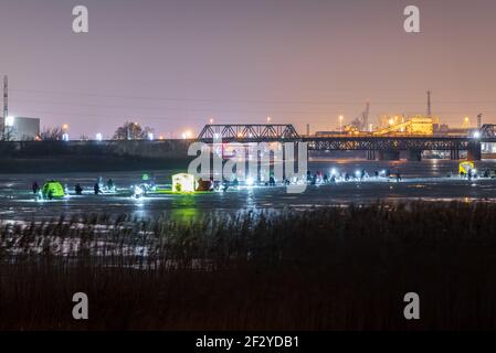 Gefrorene Fluss-, Nacht- und Eisangler fischen im Dunkeln mit künstlichem Licht und jeder sitzt einer nach dem anderen in einem Streifen mitten im Schlaf Stockfoto