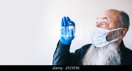 Porträt eines ausdrucksstarken bärtigen älteren Mannes, der eine medizinische Maske trägt und eine Aipula mit einem Coronavirus-Impfstoff hält. Stockfoto