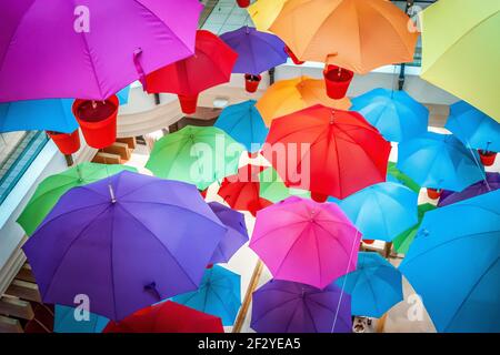 Mehrere Regenschirme in roten Töpfen an der Decke. Rot, gelb, orange, blau, pink, Violett und grün Stockfoto