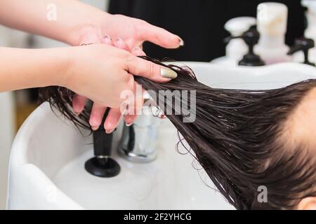 Der Friseur wäscht den Kopf eines Mädchens mit langen Haaren im Waschbecken. Braune Haare, Nahaufnahme Stockfoto