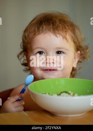 Portrait von niedlichen kaukasischen Kind Kind mit Löffel. Hungrig chaotisch Baby mit Teller nach dem Essen Püree. Stockfoto