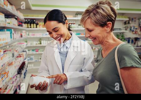 Lächelnder leitender Kunde mit Apotheker, der nach medizinischen Details zu sucht Flasche steht in der Nähe von Regalen Stockfoto
