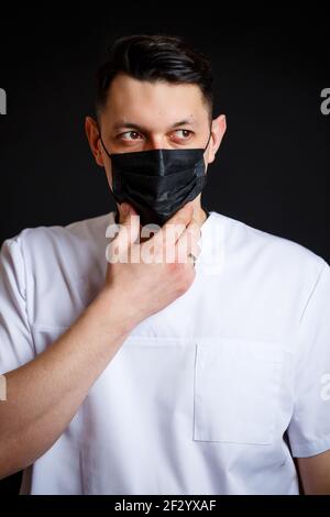 Männlicher Arzt Chefarzt in einem weißen OP-Anzug. Nahaufnahme im Hochformat. Trägt eine schwarze medizinische Maske gegen das Virus Stockfoto