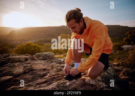 Junger Jogger bereitet sich auf den morgendlichen Lauf auf dem Bergweg gegen Sonnenaufgang am Morgen Stockfoto