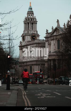 London UK Februar 2021 Vertikale Aufnahme eines Radfahrers, der sich einer Kreuzung nähert, zwei rote londoner Busse im Hintergrund. St. Pauls Kathedrale Bereich der Stockfoto