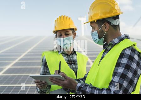 Menschen, die für alternative Energie mit Windturbine und Solar arbeiten Panel beim Tragen Gesichtsmaske während Corona Virus Ausbruch Stockfoto