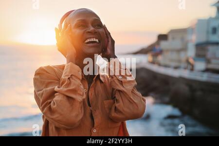 Glückliche ältere afrikanische Frau genießen Musik vor Meer während des Sommeruntergangs Stockfoto