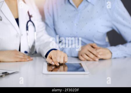 Unbekannte Ärztin zeigt ihrem Patienten eine Beschreibung der Medikamente, während sie zusammen am Schreibtisch in der sonnigen Vitrine in einer Klinik sitzt Stockfoto