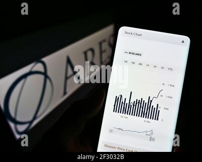 Person, die Mobiltelefon mit Webseite und Aktienkursen des US-Investors Ares Management auf dem Bildschirm vor dem Logo hält. Fokus auf der Mitte des Telefondisplays. Stockfoto