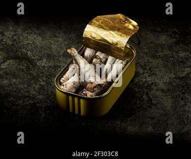 Eine gelbe Dose Sardinen in Olivenöl über einem gealterten Metalltisch in dunkler Umgebung. Stockfoto