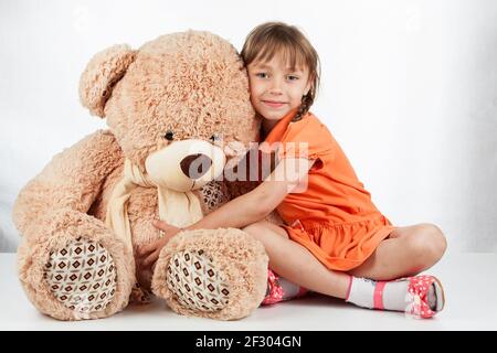 Nettes kleines Mädchen spielt mit ihrem Freund großen Pelzbär. Baby Mädchen umarmt ihren Teddybär Stockfoto