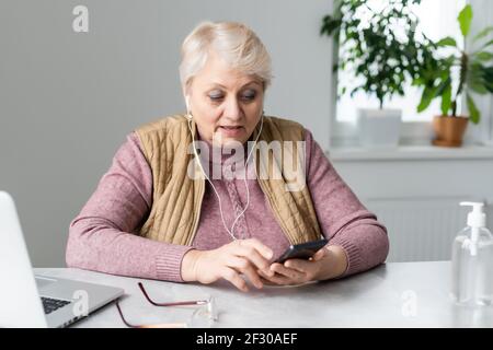 Ältere Frau am Tisch sitzend, die auf einem Smartphone tippt Stockfoto
