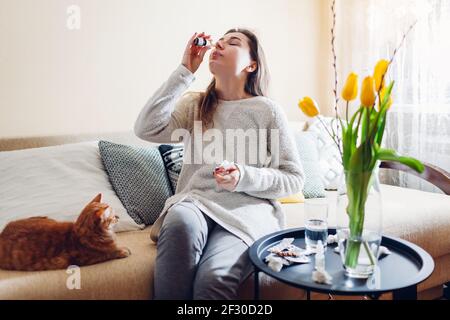 Frühjahrsallergie. Frau mit nasalen Tropfen gegen saisonale Allergie und Einnahme von Pillen zu Hause sitzen auf der Couch mit Katze. Gesundheitswesen und Medizin Stockfoto