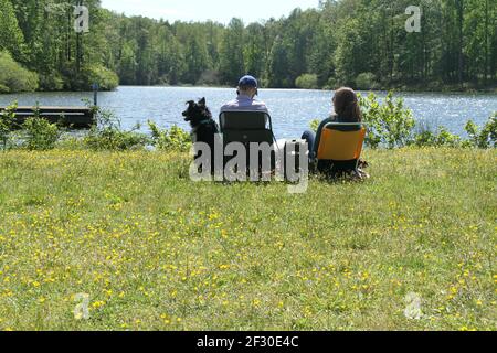 Virginia, USA. Ein Paar mit Hund sitzt an einem See an einem sonnigen Frühlingstag. Stockfoto