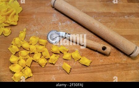 Ravioli del Plin, typische Pasta aus Langhe, Piemont, Italien - agnolotti mit Radmesser und Nudelholz auf Holzschneidebrett Stockfoto