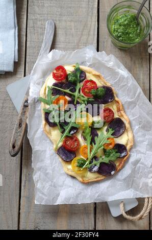 Tarte flambÃ©e mit blauen Vitelotte-Kartoffeln, bunten Tomaten, Rucola und Pesto Stockfoto