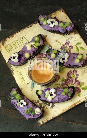 Schwarze Crostini mit Flieder-Vitelotte-Kartoffelcreme-Käse, Zwiebel und gehörnter Stiefmütterchen Stockfoto
