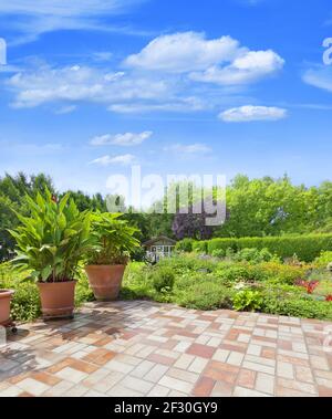 Schöne, gepflegte Gartenterrasse mit buntem Blumenbeet und Gartenteich. Stockfoto