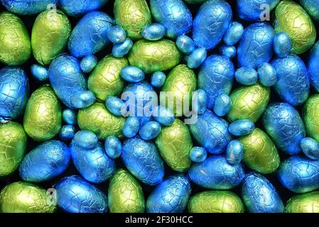 Stapel oder Gruppe von mehrfarbigen und verschiedenen Größen von bunten Folie verpackt Schokolade ostereier in blau, gelb und lindgrün. Stockfoto