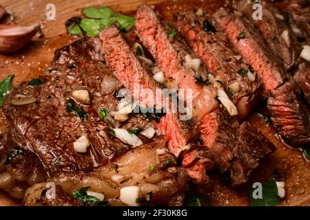 Frisch gebratenes, mittelseltenes Sirloin-Steak auf dem Schneidebrett, das in Butter, Knoblauch, Schalotte und Petersilie gebraten ist Stockfoto