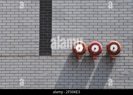 Nahaufnahme von drei roten Sprinkleralarmen, die an einem montiert sind Graue Ziegelwand Stockfoto