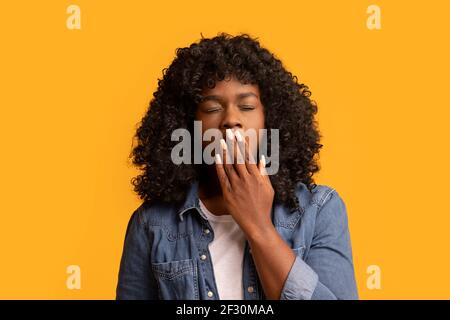 afroamerikanische Frau, die auf gelb gähnt und den Mund mit der Hand bedeckt Stockfoto