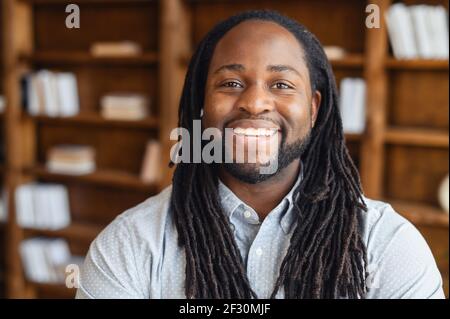 Porträt-Nahaufnahme eines lächelnden jungen, gutaussehenden afroamerikanischen Mannes mit Dreadlocks, der in der Bibliothek posiert oder die Kamera anschaut, ist der optimistische Büroleiter des schwarzen Mannes bereit zur Arbeit Stockfoto