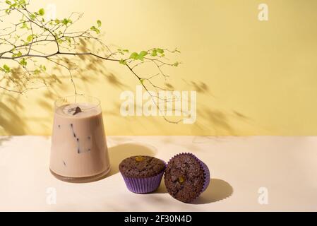 Iced Coffee Latte mit Schokolade Cupcakes auf dem gelben Hintergrund in Sonnenlicht, erfrischende Sommergetränk, Sommer-Frühstück. Stockfoto