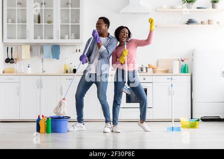 Fröhlicher junger Mann und Frau imitieren Rockstars während der Haushaltung Stockfoto