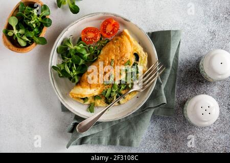 Omelette gefüllt mit Tomaten, rotem Paprika, Frischkäse und Mais oder Lammsalat auf hellem Beton Hintergrund mit Kopierraum. Gesunde Ernährung Lebensmittel Stockfoto