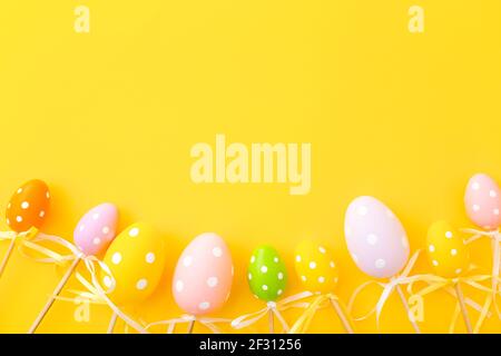 Bunte Ostereier auf Stöcken auf gelbem Hintergrund. Festliche Osterfeiertage Grußkarte mit Kopierplatz. Stockfoto