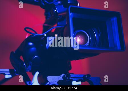 Moderne digitale Cinema-Kamera mit Moto Zoom Teleobjektiv in Blau und Rot Film Bühnenbeleuchtung Nahaufnahme angebracht. Ausrüstung Für Die Filmindustrie. Stockfoto