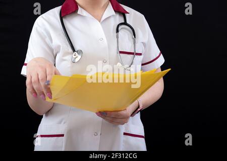 Ärztin mit Stethoskop und Dokumentenmappe auf dunklem Hintergrund, Nahaufnahme Stockfoto