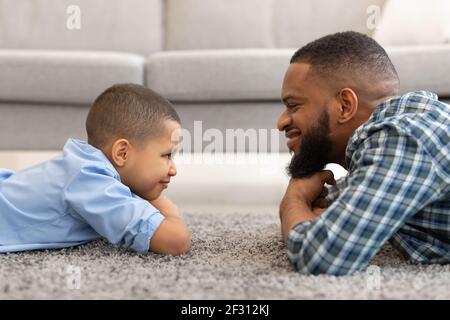 Afrikanischer Vater Und Sohn Liegen Zu Hause Auf Dem Boden, Seitenansicht Stockfoto