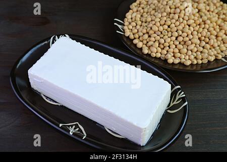Nahaufnahme eines weichen Tofu Bean Curd mit verschwommen getrocknet Sojabohnen stapeln sich im Hintergrund Stockfoto