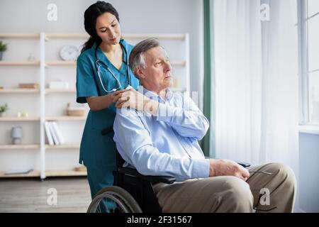 Junger Arzt hält ältere behinderte männliche Hand, ihm Unterstützung im Altersheim Stockfoto