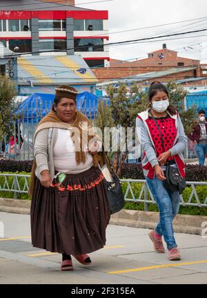 El Alto, La Paz, Bolivien - Februar 11 2021: Bolivianische indigene Frau, bekannt als 'Cholita', läuft mit einer jungen Frau, die eine Maske trägt Stockfoto