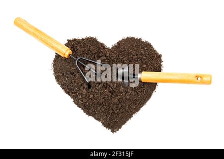 Garten Handtransplanter und Grubber in einem herzförmigen Haufen Erde isoliert auf weißem Hintergrund. Gartenarbeit Leidenschaft Konzept. Stockfoto